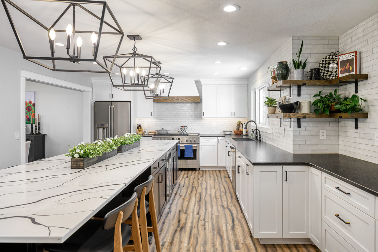 A remodeled kitchen by Compelling Homes featuring an oversized marble island, open shelving, and a subway tile backsplash.