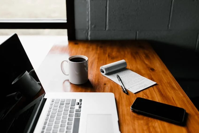 Laptop on desk with coffee cup, phone, and notepad